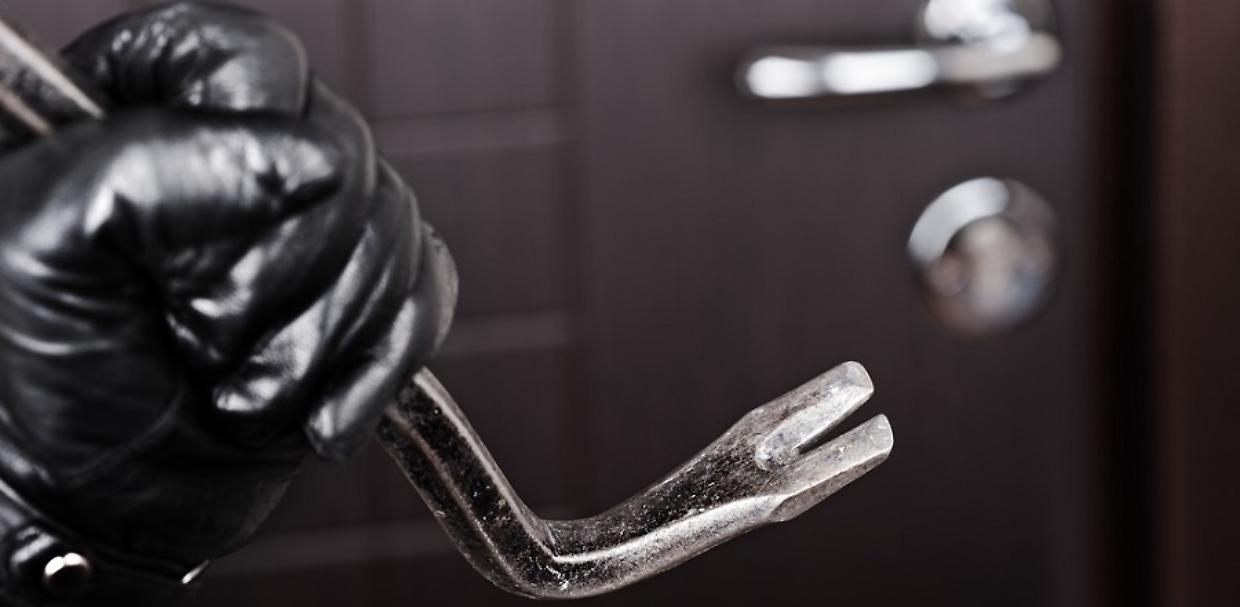 Burglar hand holding crowbar break opening door
