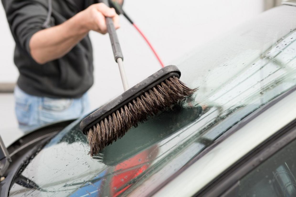 Car washing. Man cleaning car using high pressure water and brus