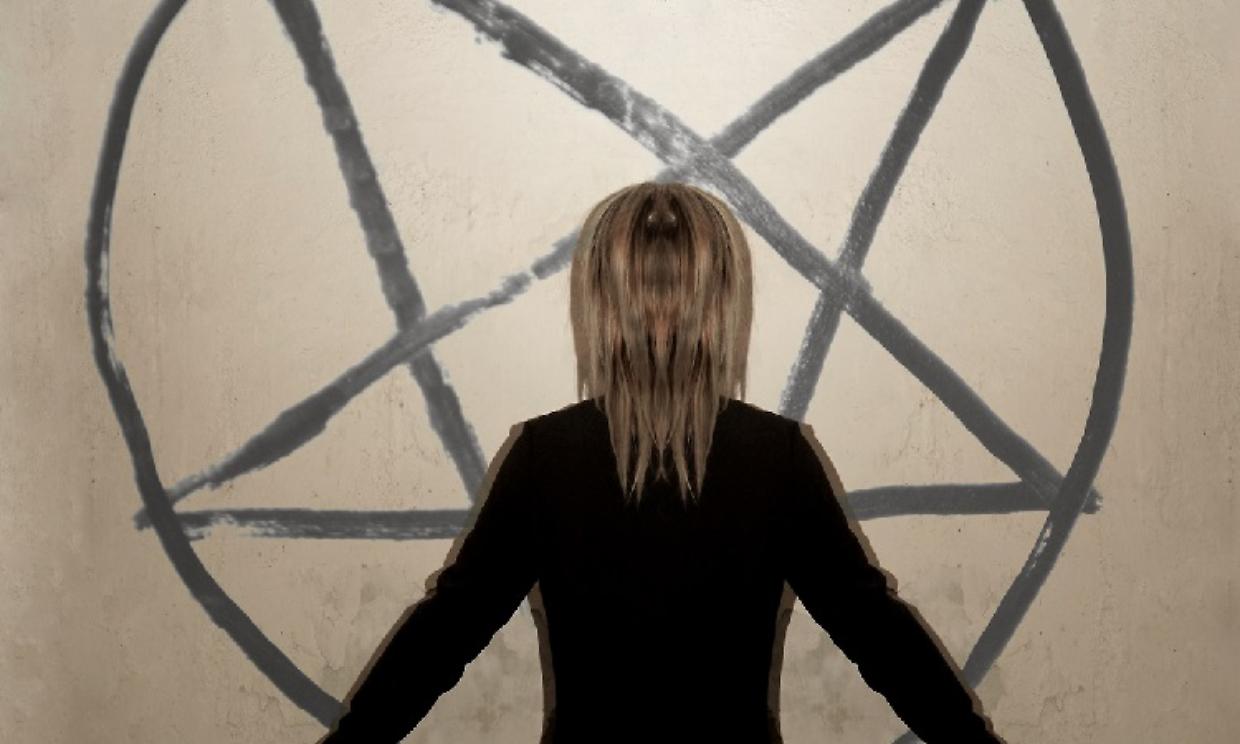 girl stands near the gray wall with painted pentagram in round.
