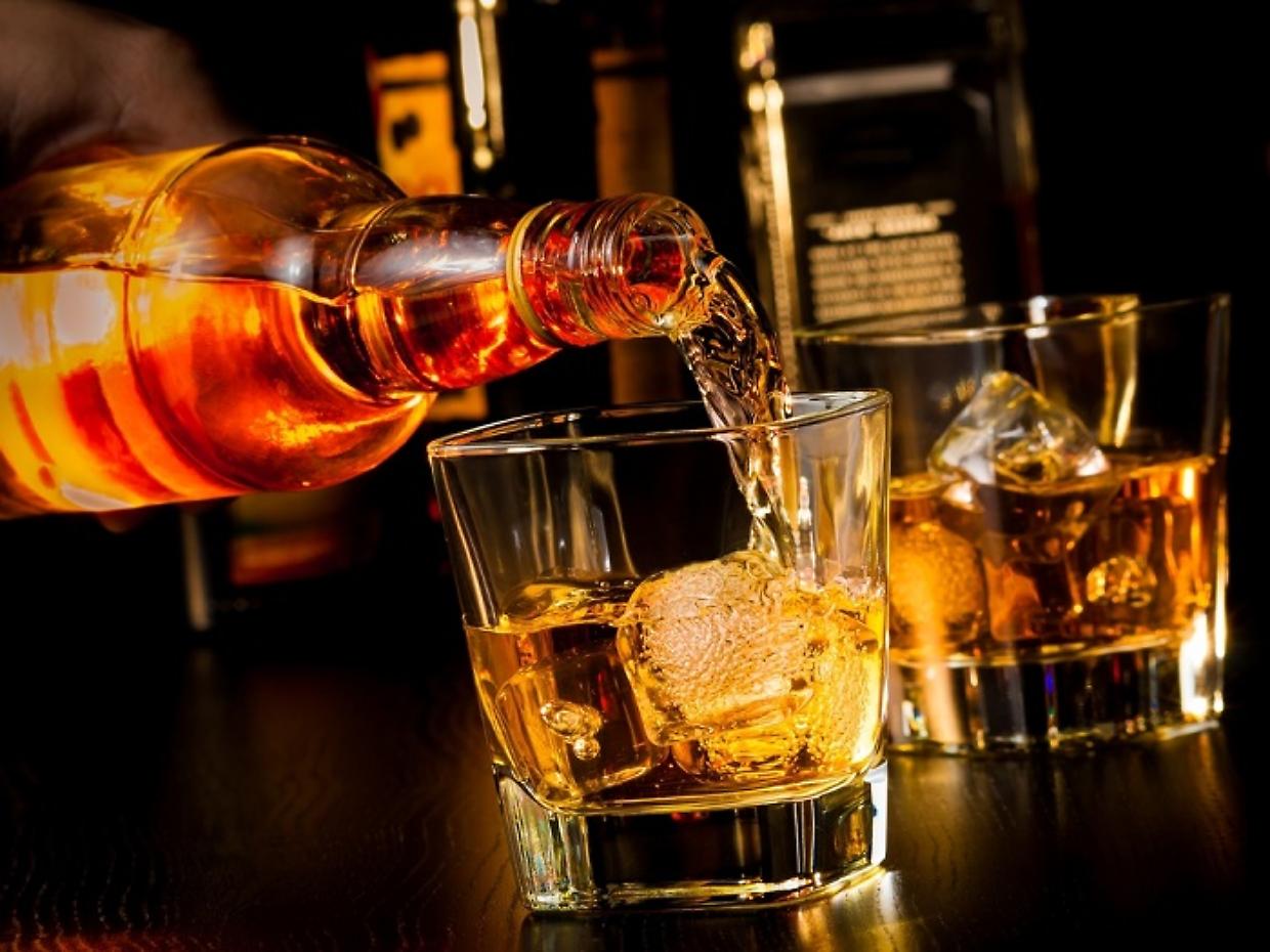 barman pouring whiskey in front of whiskey glass and bottles