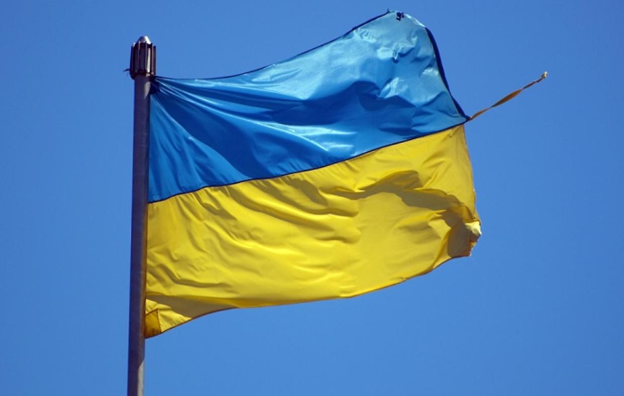 big torn Ukrainian flag flutters in wind against blue sky