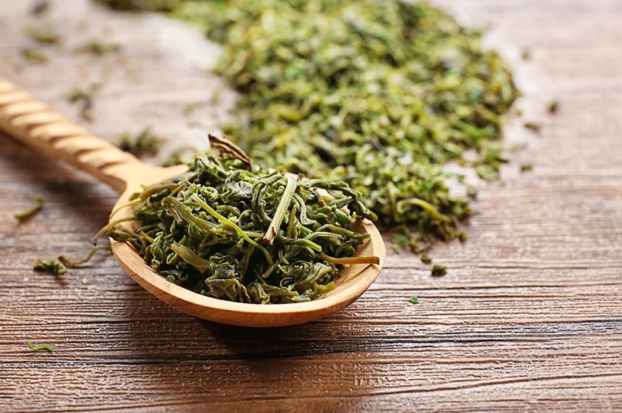 Dry tea leaves in wooden spoon on table
