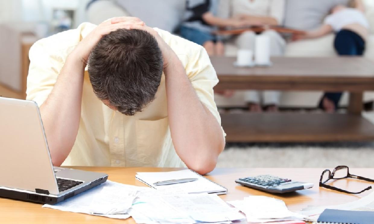 Man calculating his bills while his family are on the sofa