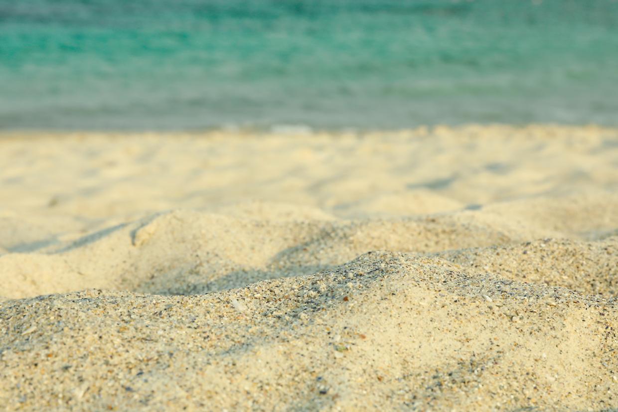 Sea sand against blue sea water, space for text. Summer backdrop