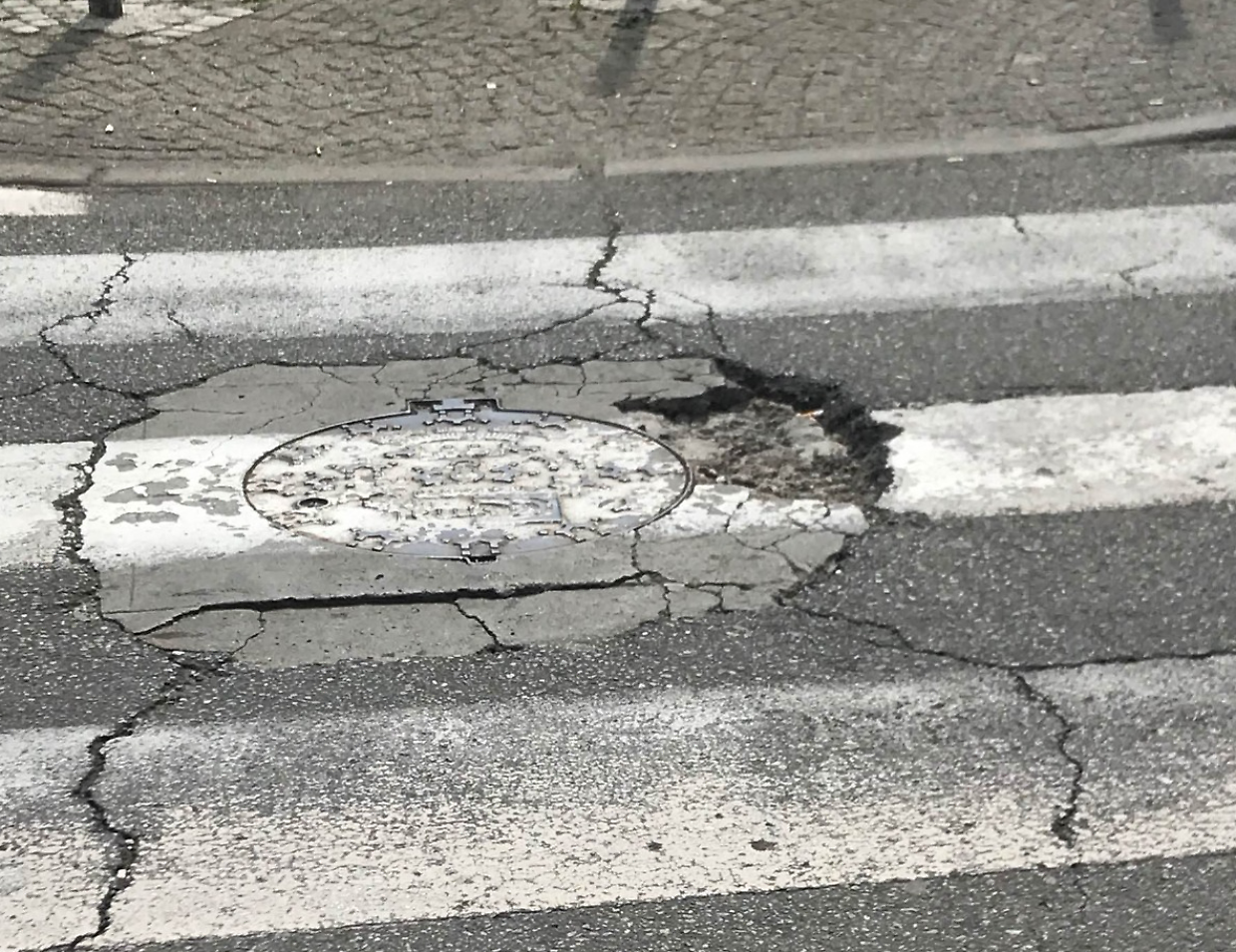 Una grossa buca nell'asfalto, proprio in prossimit&agrave; delle strisce pedonali