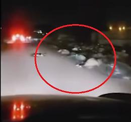 In strada, di notte: sull'asfalto e ai lati della carreggiata c'è un tappeto di rifiuti