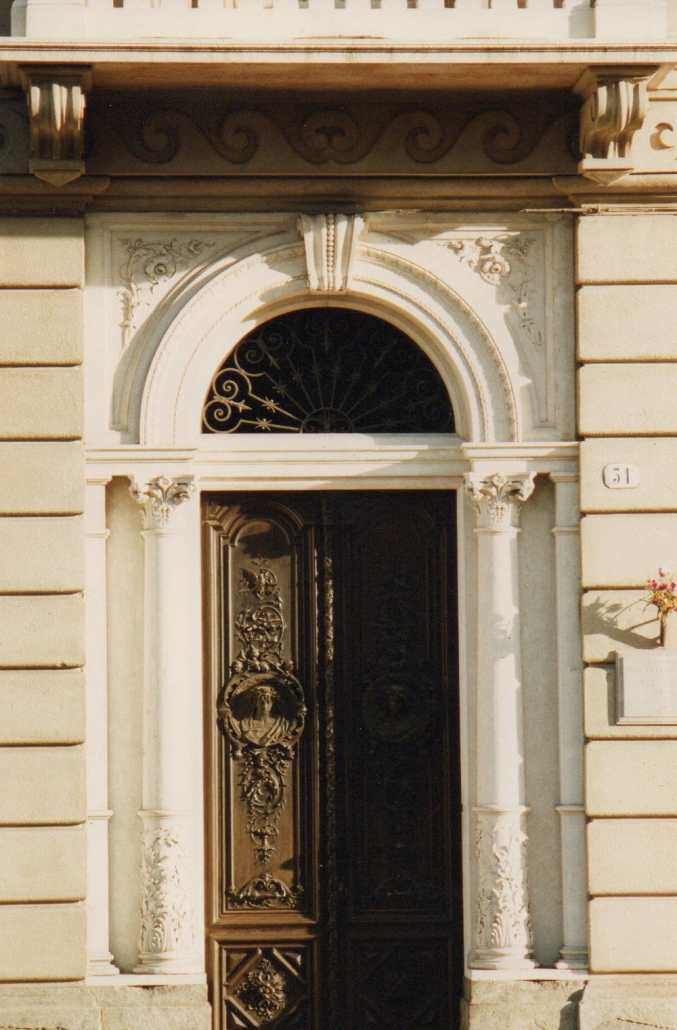 Tra gli elementi più riconoscibili c’è il portone in legno dell’ingresso residenziale, arricchito da rilievi/medaglioni in bronzo: si tratta di decorazioni legate direttamente alla produzione dell’artista, per le quali esistono anche modelli preparatori catalogati nel patrimonio culturale